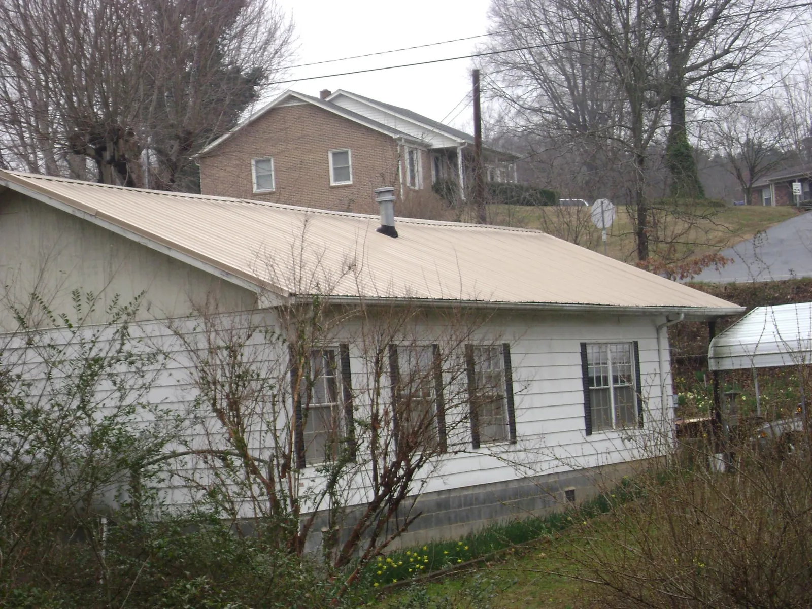 Tan metal roof on a white sided house set into a hillside — Commercial Roofing by Roofing Brothers in Albany